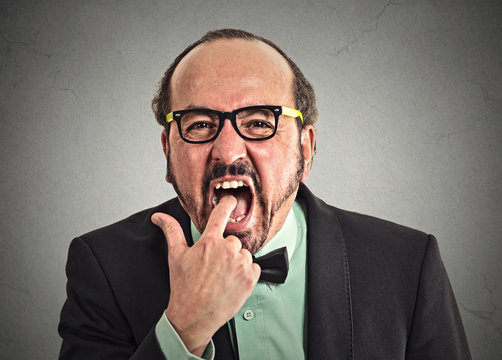 disgusted man with finger in mouth on grey wall background 