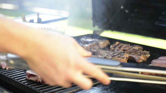 A man grills lamb chops on the outdoor barbeque