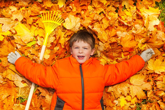 Boy laying on the autumn leaves with rake