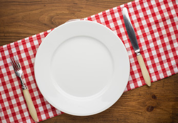 Empty plate with fork and knife on tablecloth over wooden