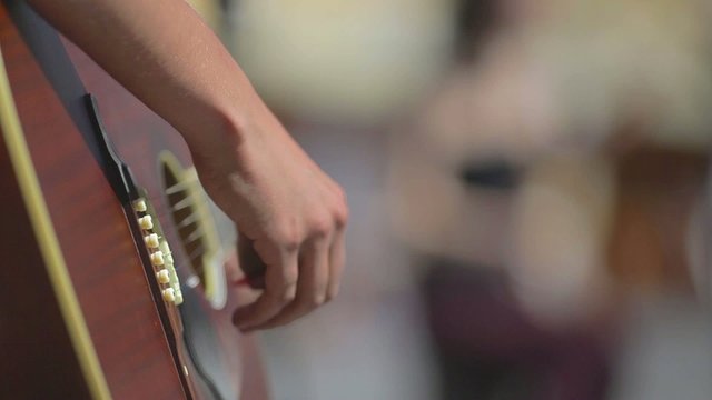 Playing on a brown guitar at daytime on the street