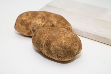 Fototapeta na wymiar Two Potatoes on White Counter with Wood Board