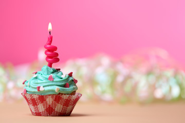 Delicious birthday cupcake on table on pink background