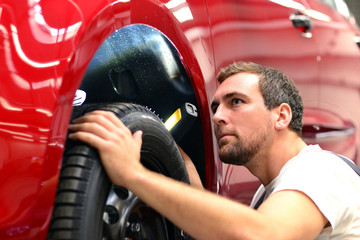 KFZ Mechaniker kontrolliert Reifen und Fahrzeug in d. Werkstatt