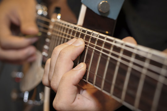 Man with his fingers on the frets of a guitar