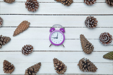 Alarm clock and pine cone spruce on a wooden table.