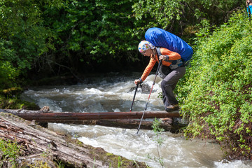 Backpacker is crossing mountain river by wooden log in Altai mou