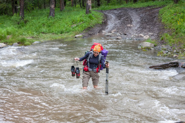 Backpacker is crossing mountain river barefoot in Altai mountain