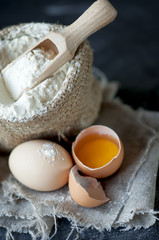 flour  in burlap with wooden spoon and eggs  on a gray cloth
