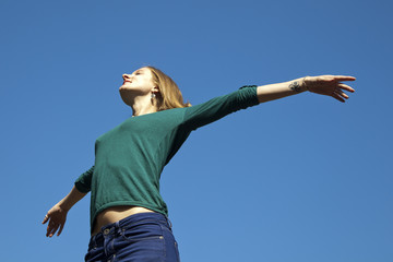 Chica rubia con jersey verde abriendo los brazos al cielo