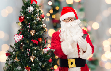 santa claus with smartphone and christmas tree