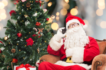 santa claus with smartphone and christmas tree