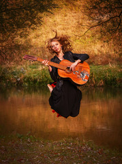Fototapeta premium Young woman jumping with guitar