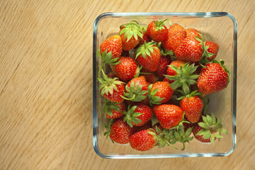 Strawberry fruit in a glass container on a wooden surface. Bokeh