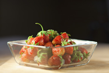 Strawberry fruit in a glass container on a wooden surface with d