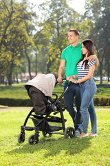 Fototapeta premium Young parents pushing a baby stroller in park