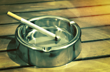 Metal ashtray with a cigarette on a table