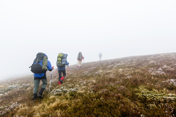 Group of hiker are walking in mountains covered with dense cloud
