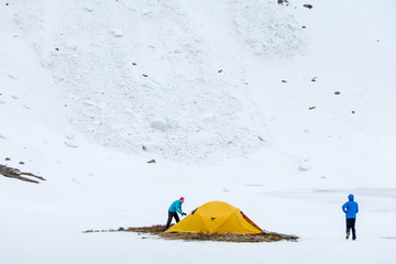 Hikers set oragne tent in winter mountains on cloudy day