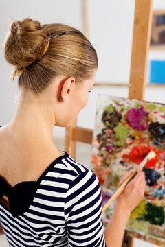 Female art student working over picture at easel in university