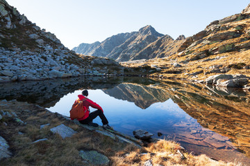 Male hiker takes a rest sitting next a mountain lake - obrazy, fototapety, plakaty