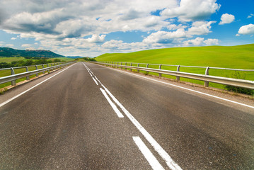 Long way between green fields with blue sky in the background