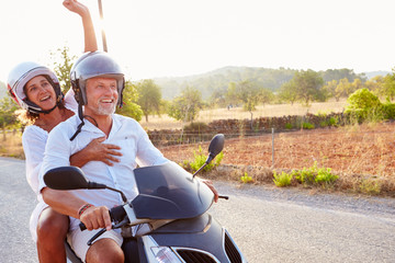 Mature Couple Riding Motor Scooter Along Country Road