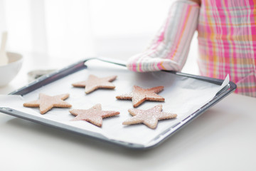 close up of woman with cookies on oven tray