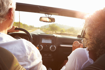 Mature Couple Driving Along Country Road In Open Top Car