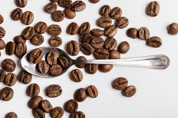 Teaspoon and coffee beans on white