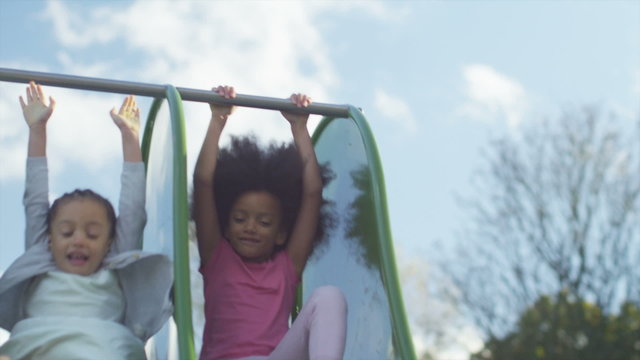 Two Young Children Playing On A Slide In A Playground