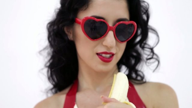 Hot brunette woman with red glasses sexy eating banana