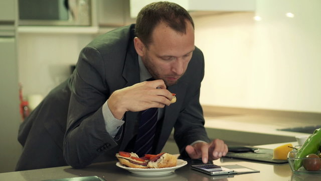 Businessman texting, sending sms on smartphone and eating sandwi