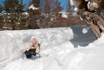 Fototapeta na wymiar Little girl on a sled sliding down a hill in the snow in winter