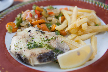 Grilled fish, chips and salad on the plate