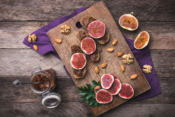 Sliced figs, nuts and bread with jam on choppingboard in rustic