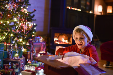 Lovely little boy with a santa claus hat opens a gift in front o