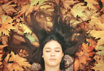Portrait of beautiful brunette woman lying on maple leaves