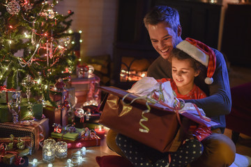 Lovely little girl with a santa claus hat and her father opening