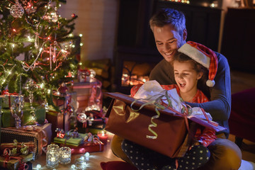 Lovely little girl with a santa claus hat and her father opening