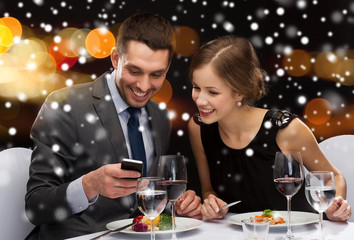 smiling couple with smartphone at restaurant
