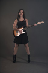 Teenage rock girl with electric guitar. Wearing black dress.