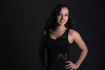 Smiling cute brunette teenage girl wearing black dress. Studio f