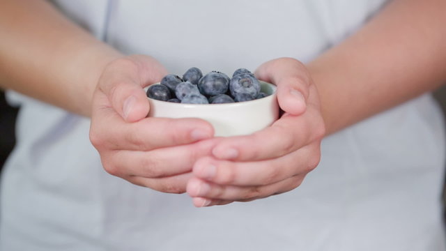 female teen hand show bowl full of blueberries, made from raw