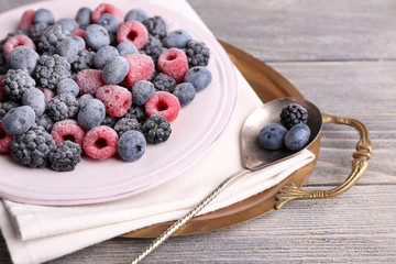 Iced berries on plate, on color wooden background