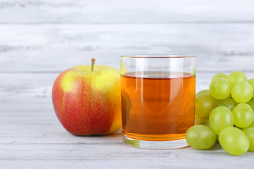 glass of juice with fresh grape and apple on grey wooden table