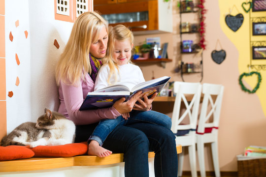 Mutter liest Tochter ein Buch vor in K&uuml;che