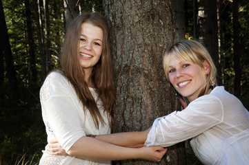 Fototapeta premium Environmental Portrait of two women hugging a tree in a forest