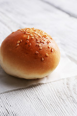 Tasty bun with sesame on color wooden background