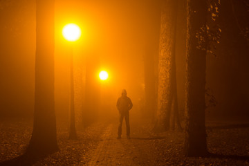 Man alone standing in the middle of a lane on a foggy night.